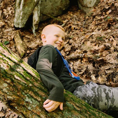 Young boy holding on to a log while laying in leaves.