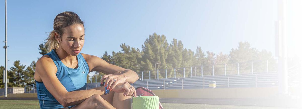 Women wearing a blue tank top sitting on the ground turning off her Apple Watch.