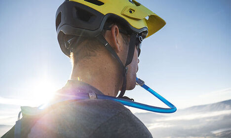 Man drinking from a Camelbak reservoir valve with a bike helmet on.