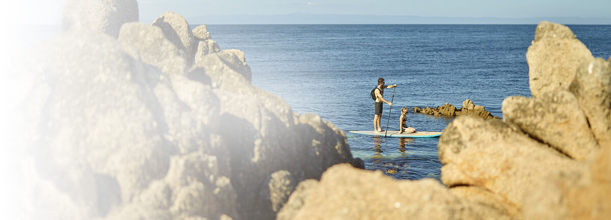 Two people on a paddle board, cruising along a rocky coast.
