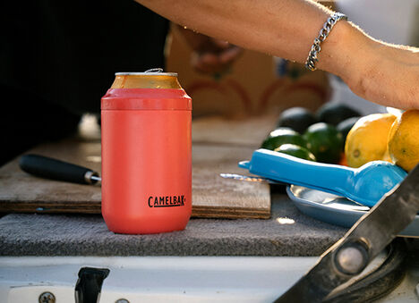 A can cooler on an outdoor table with lemons and limes being cut in the background