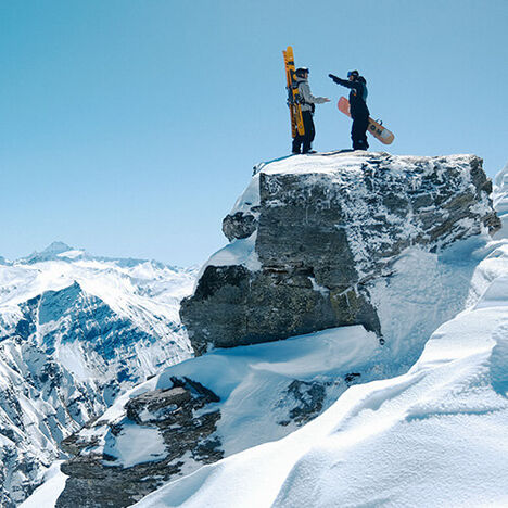 Two boarders sitting atop a snowy peak