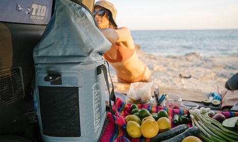 Woman reaching in to her ChillBak™ Soft Cooler with fruit and veggies beside it.