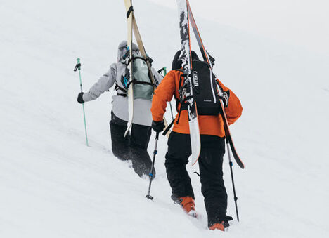 People walking up a mountain with their skis on their CamelBak hydration packs.