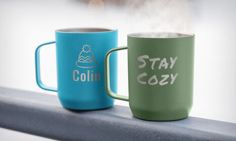 Two mugs laser engraved with text and logo sitting on a railing. Two mugs laser engraved with text and logo sitting on a railing.