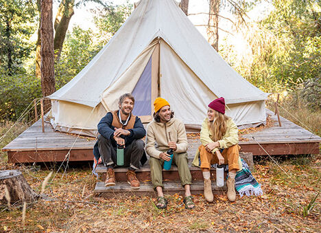 Group of three people with water bottles in front of a tent. Group of three people with water bottles in front of a tent.
