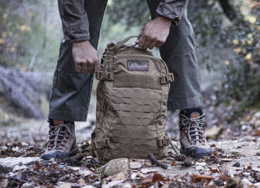 man standing on a trail covered in leaves with a backpack on the ground