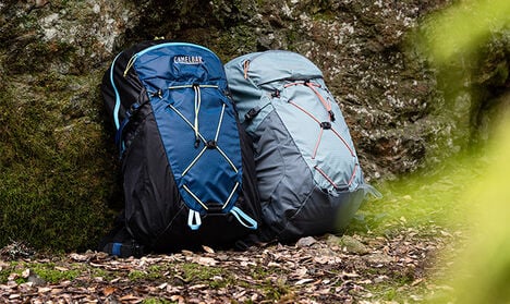 Two Fourteener hydration packs sitting against a rock in the woods.