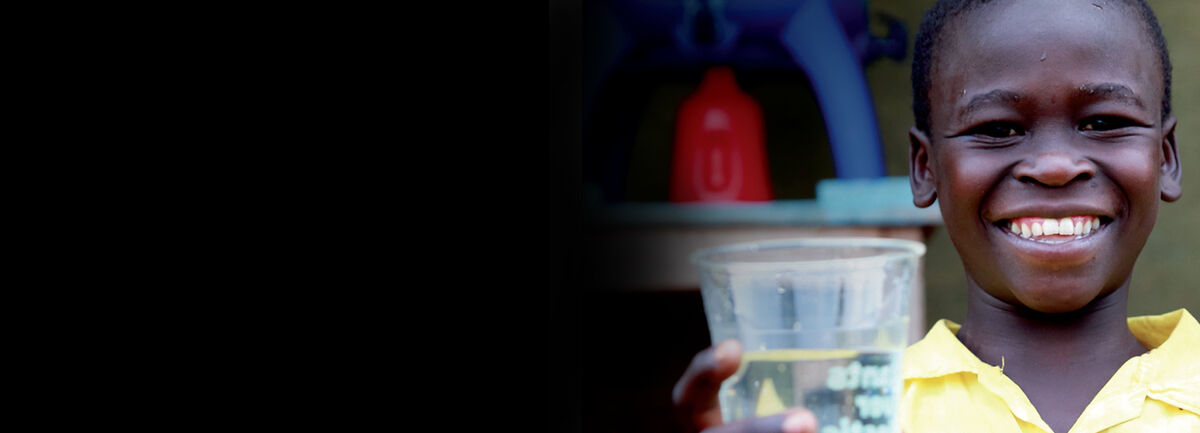 Small child smiling and holding a glass of water. 
