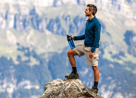 Guy on the top of a rocky summit, overlooking the view ahead.