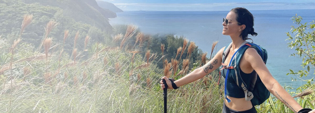 Sophia Amoruso standing outside with sunglasses on and hiking poles in her hands.
