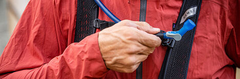 Man grabbing his hydration tube from his pack..