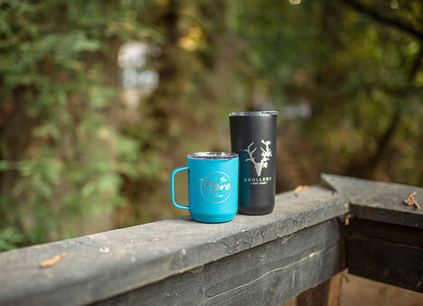 Two custom stainless steel coffee mugs on a porch rail
