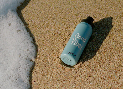 Dusk Blue Chute Mag water bottle on the sand with the tide rolling in on the left.
