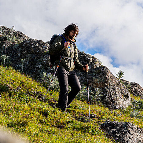 Hiker going down a hill with a hydration pack and hiking poles.
