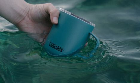 Lagoon Camp Mug in the water with a hand holding on to it.