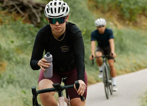 Two cyclists riding down a paved path while the one in the front holds on to a Podium Steel water bottle.