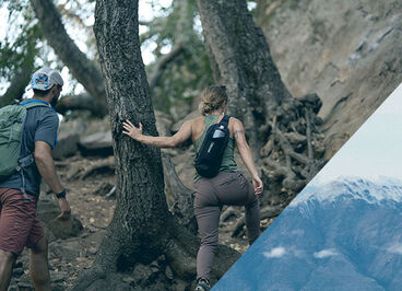 A woman hiking near a tree wearing an Arete sling.