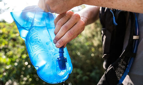 Guy with a pack on filling his Camelbak reservoir with water.