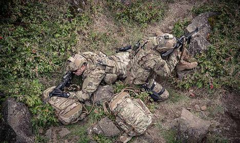Two soldiers laying prone on their hydration packs.
