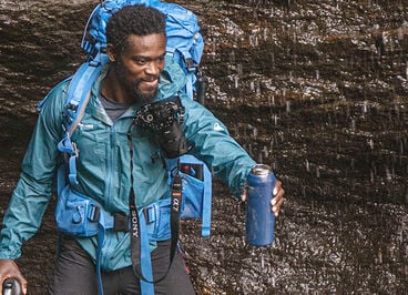 Man in hiking gear collecting falling water in water bottle.