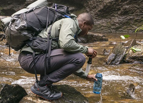 Hiker wearing a hydration backpack and filling up Lifestraw bottles in a stream. Hiker wearing a hydration backpack and filling up Lifestraw bottles in a stream.