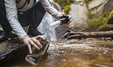 Person putting water from a river in their CamelBak filtered by LifeStraw water bottle. 