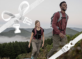 Two hikers going up a trail with smiles and hydration packs on.