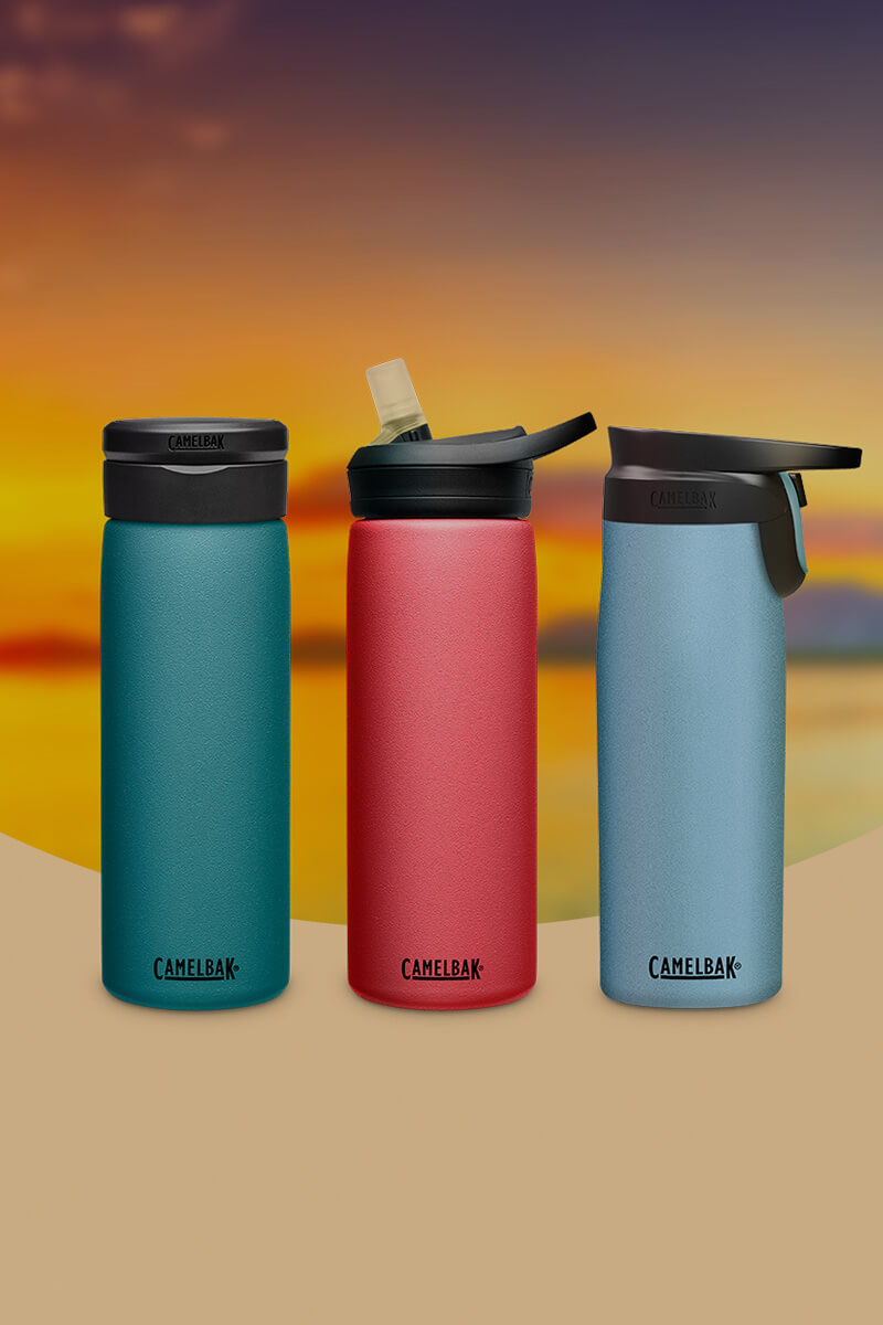 Three bottles in Lagoon, Wild Strawberry, and Dusk blue with a sunset scene behind them.