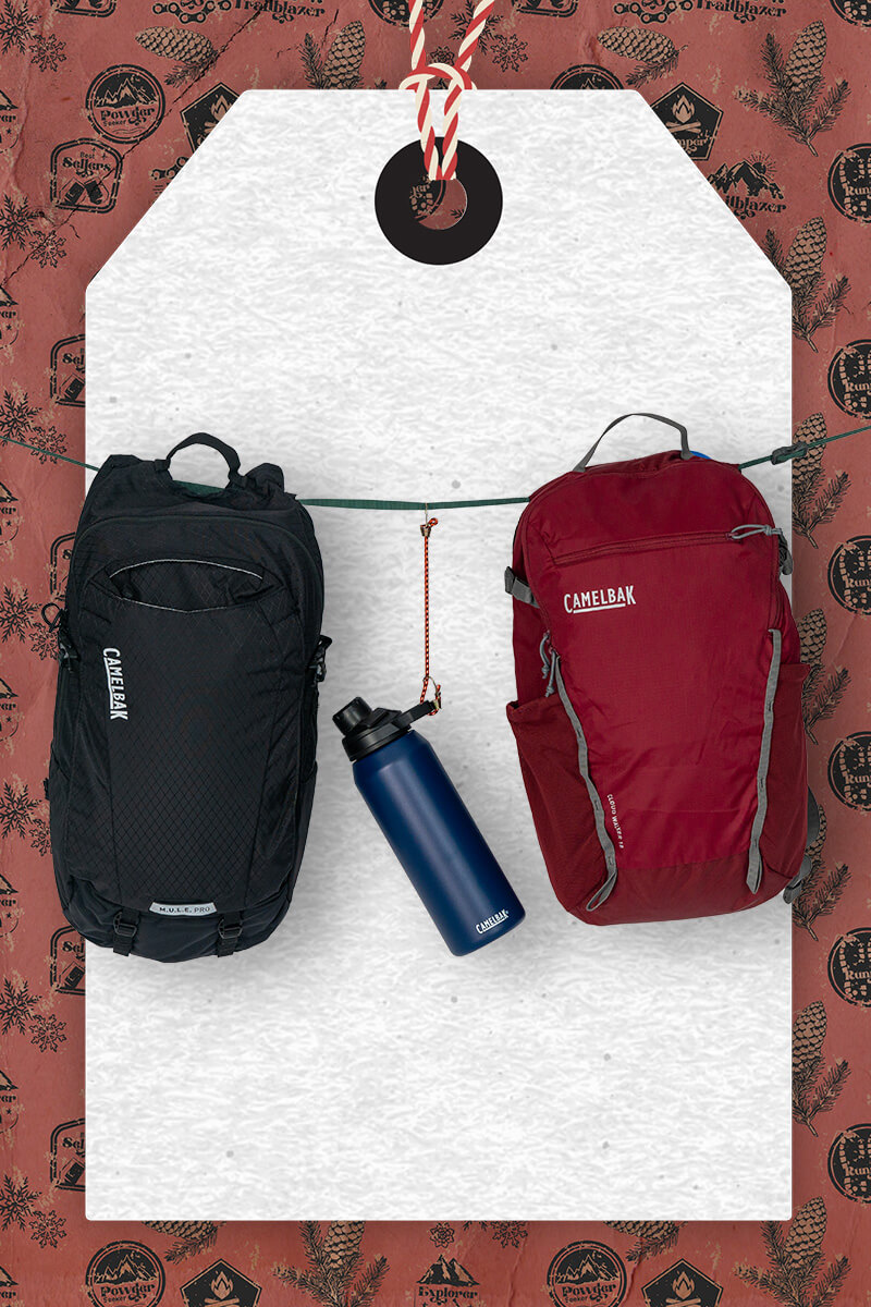 Two hydrations packs and a water bottle hanging in front of a holiday-themed hang tag with wrapping paper in the background.