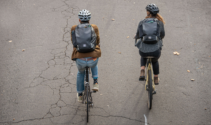 Two people riding their bikes wearing commute packs.