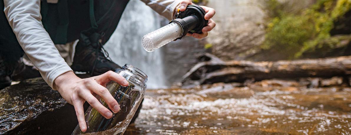 Person holding a CamelBak filtered by LifeStraw water bottle and collecting water from a stream.