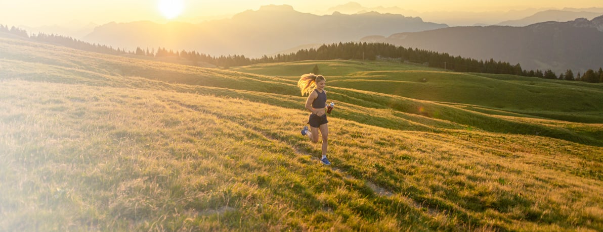 Women running through a field holding a water bottle while the run is rising. 