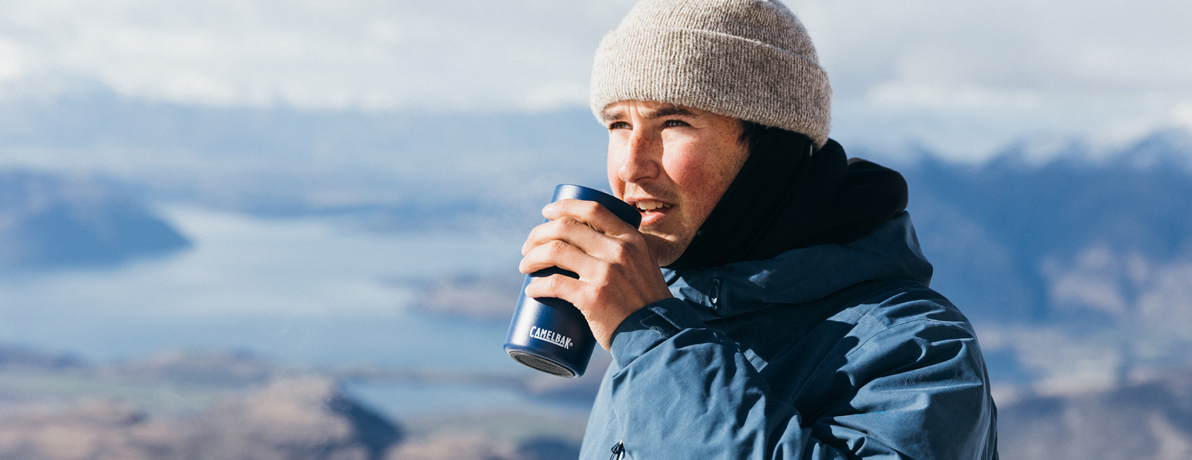 Man with a winter hat and jacket on about to take a sip out of a CamelBak tumbler.