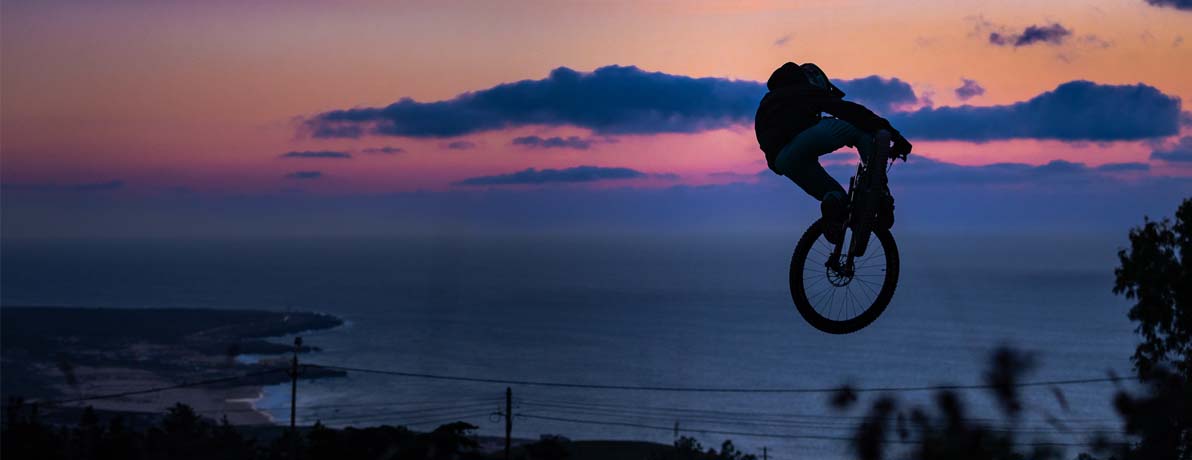 Mountain biker hitting a jump while a sun is setting in the distance.