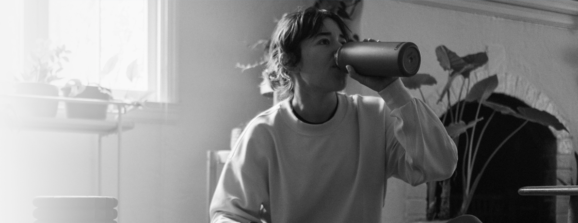 Black and white photo of a women sitting on the floor drinking from a CamelBak stainless steel water bottle.