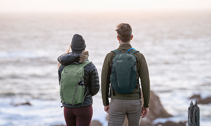 Two people wearing a hydration backpacks looking out over the water.. Two people wearing a hydration backpacks looking out over the water..