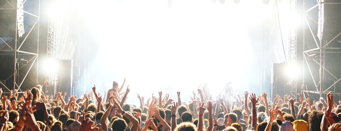 Stage at a festival with crowd in front of the stage with hands in the air clapping and dancing.