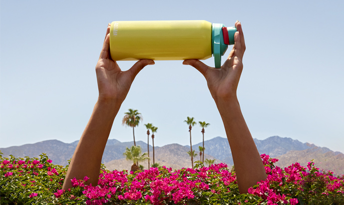 Yellow stainless steel water bottle being held up with palm trees in the background. Yellow stainless steel water bottle being held up with palm trees in the background.