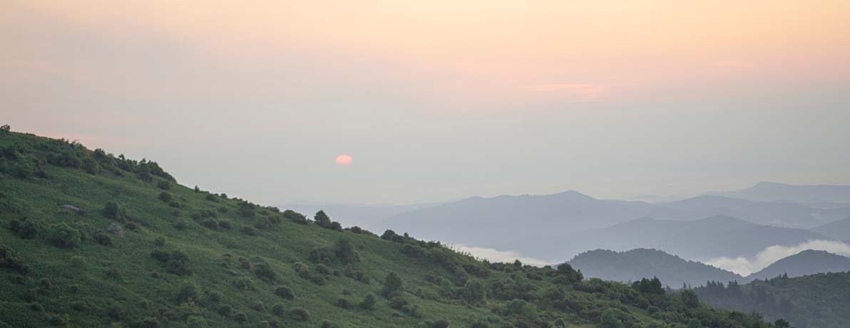 Landscape imagery of green mountains and the sun is starting to set. 