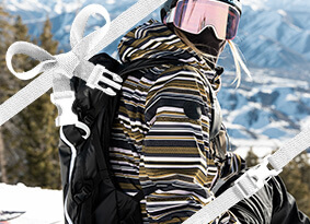 A snowboarder geared up at the top of the slope, glancing towards the camera before she goes down the mountain.