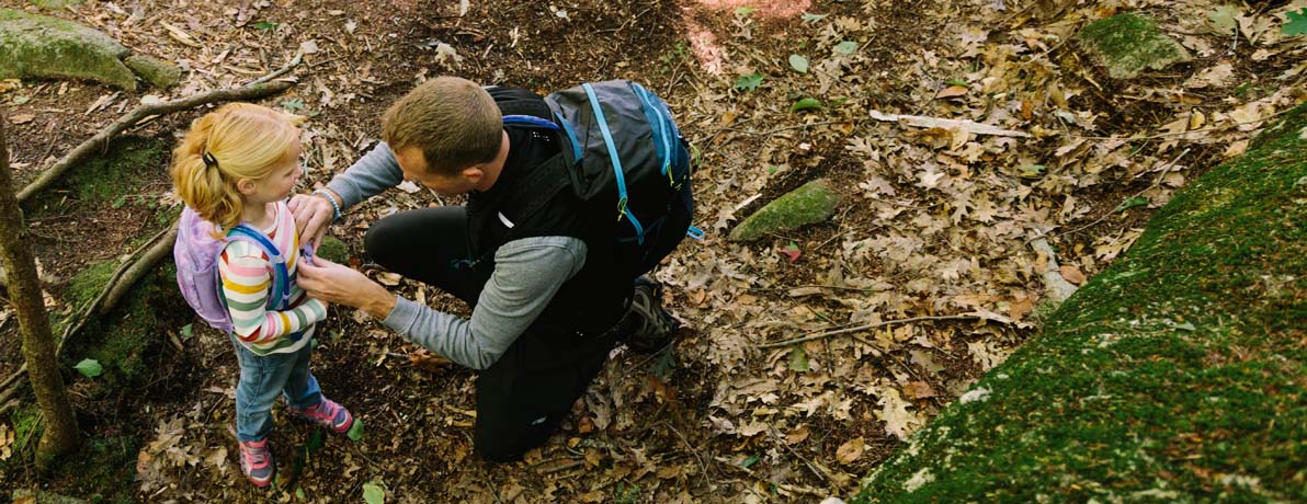 Father and daughter stopping to check gear while on a hike in the woods.