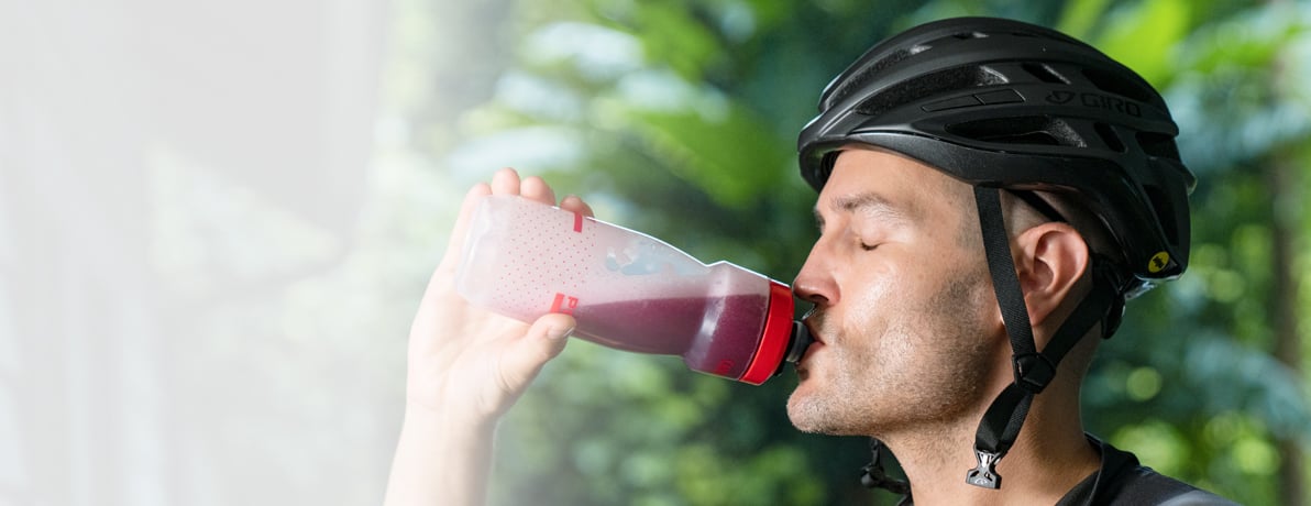 Man wearing a helmet taking a drink out of a Podium water bottle.